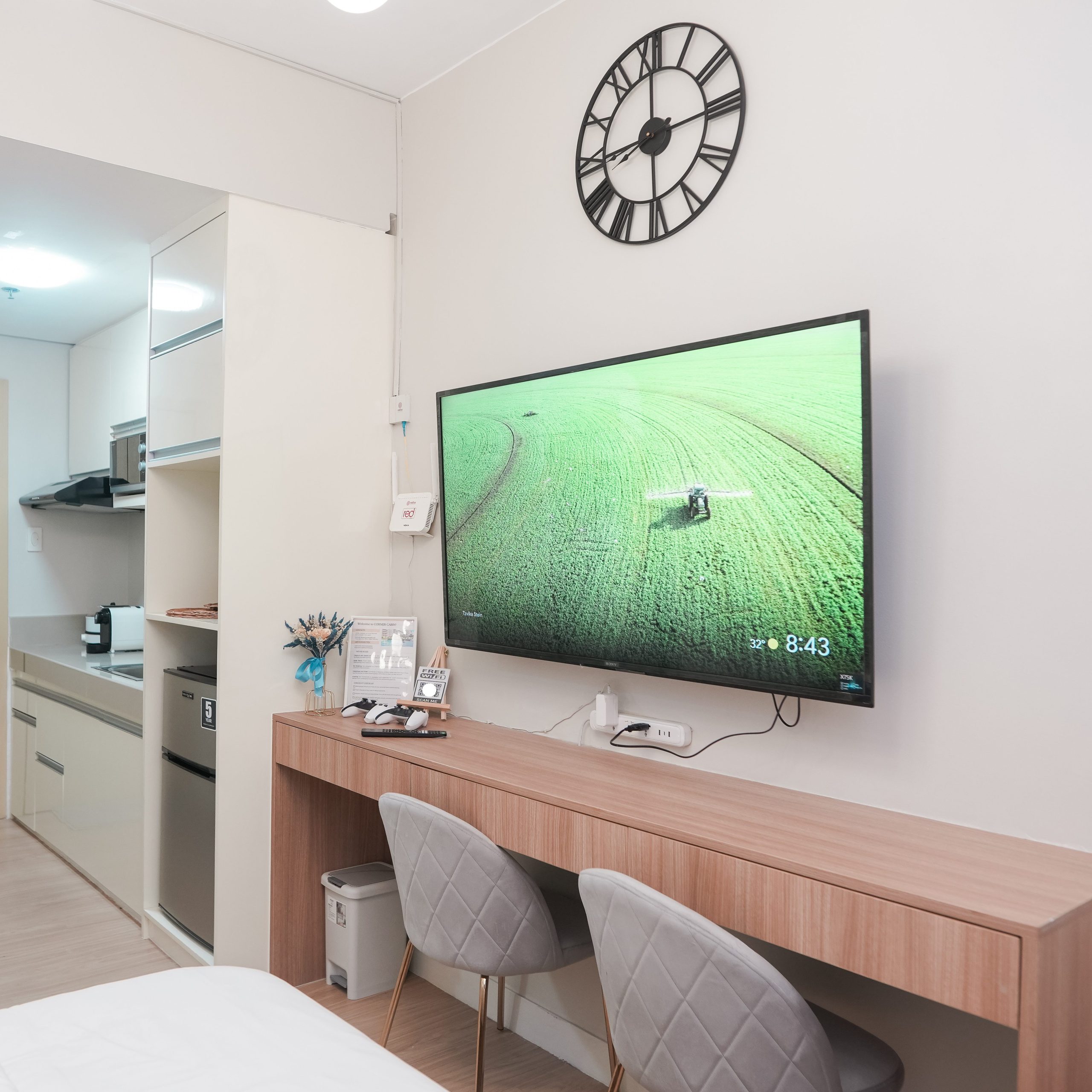 A long table and two chairs below the 55-inch smart TV mounted on the wall. The table is multi-purpose, and can be used as a dining table or a workstation.