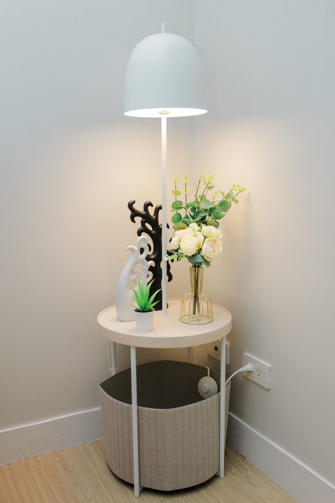 At Corner Cabin - Trees Residences, on the bed's side table, there's a white vase filled with white flowers and green foliage, accompanied by a black and white prosperity tree.